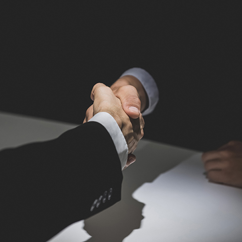 Anonymous business partners making handshake in dark shadow