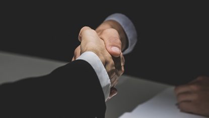 Anonymous business partners making handshake in dark shadow
